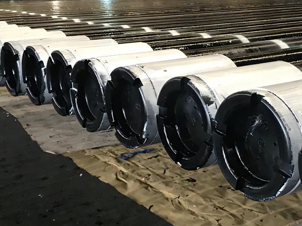 A row of drill pipes with black thread protectors on the ground